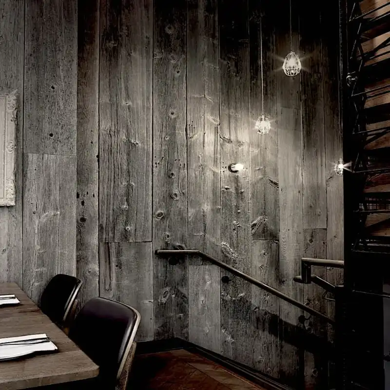  Intérieur de restaurant faiblement éclairé avec murs en panneaux de lambris bois ancien, un escalier et une table à manger avec des chaises et des serviettes. 