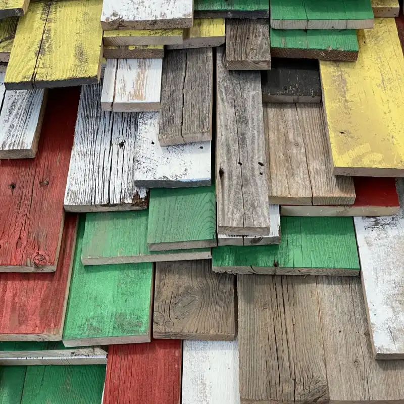  Vue rapprochée d'un mur recouvert de planches de bois superposées et patinées, le vieux bois coloré peint dans diverses nuances délavées, notamment le rouge, le vert, le jaune et le blanc. 