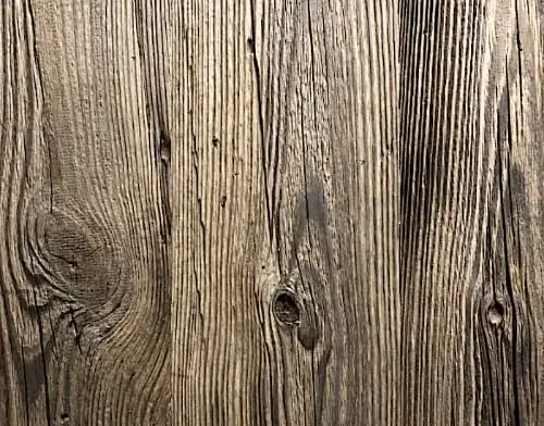 Gros plan d'une planche de bois brun patiné avec des rainures visibles, des nœuds et une texture rugueuse, mettant en valeur le charme rustique du bardage bois ancien brun.