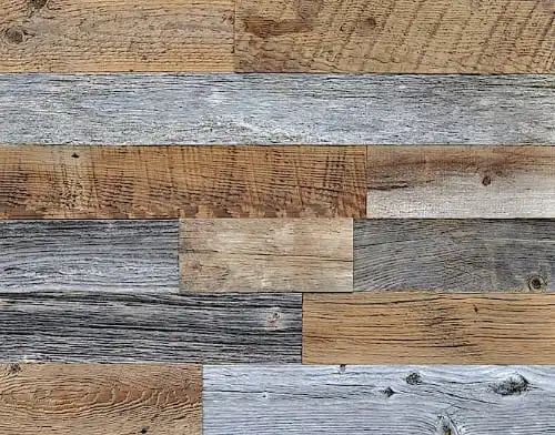 Vue rapprochée d'un mur en planches de bois multicolores disposées en quinconce. Les planches, rappelant le bois de grange, varient en couleur du gris clair au brun foncé, mettant en valeur différents grains et textures de bois.