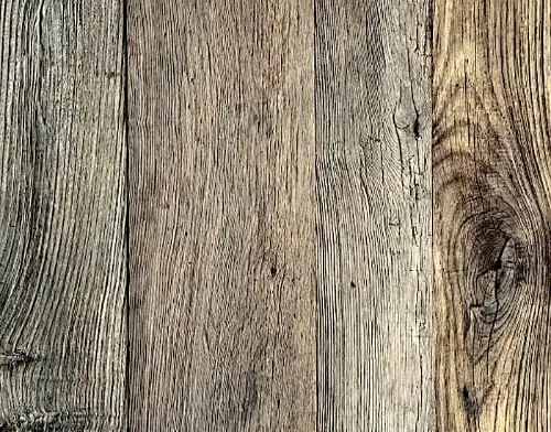 Vue rapprochée de planches de bois patinées dont le grain et la texture sont visibles. Le bardage vieux châtaignier varie en couleur du brun clair au gris et présente des nœuds et des fissures naturels.