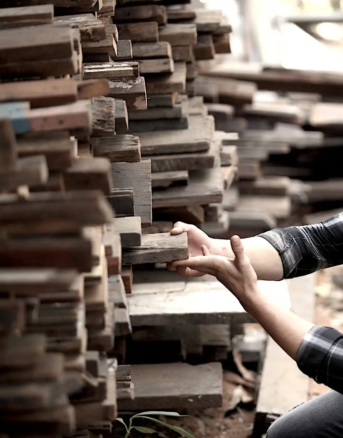 Les mains d'une personne sélectionnant un morceau de vieux bois parmi un gros tas de planches de bois empilées.