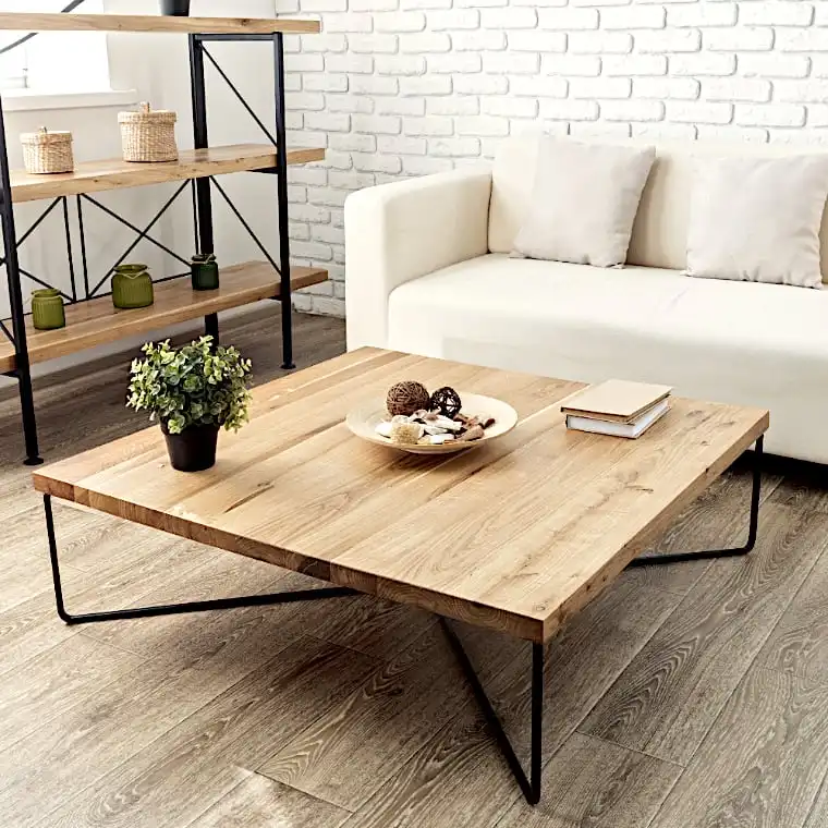  Un salon moderne comprend une table basse en bois avec des pieds en métal, rappelant une table basse en bois ancien, un canapé blanc, une plante en pot et une étagère avec des objets décoratifs contre un mur de briques blanches. 