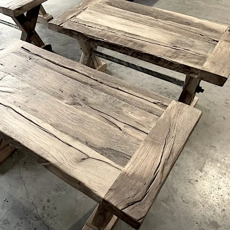  Deux tables rustiques en bois avec des motifs de grains visibles et des imperfections naturelles sont placées sur un sol en béton. Ces pièces de table en bois rustique comportent des pieds croisés robustes, ajoutant un charme intemporel à n'importe quel espace. 