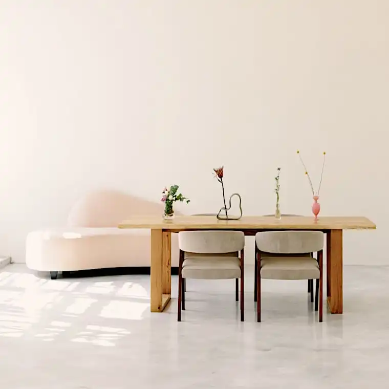  Une pièce minimaliste avec une table vieux bois, quatre chaises de couleur claire et des vases décoratifs simples. Un canapé de couleur crème se trouve en arrière-plan, contre un mur uni. 