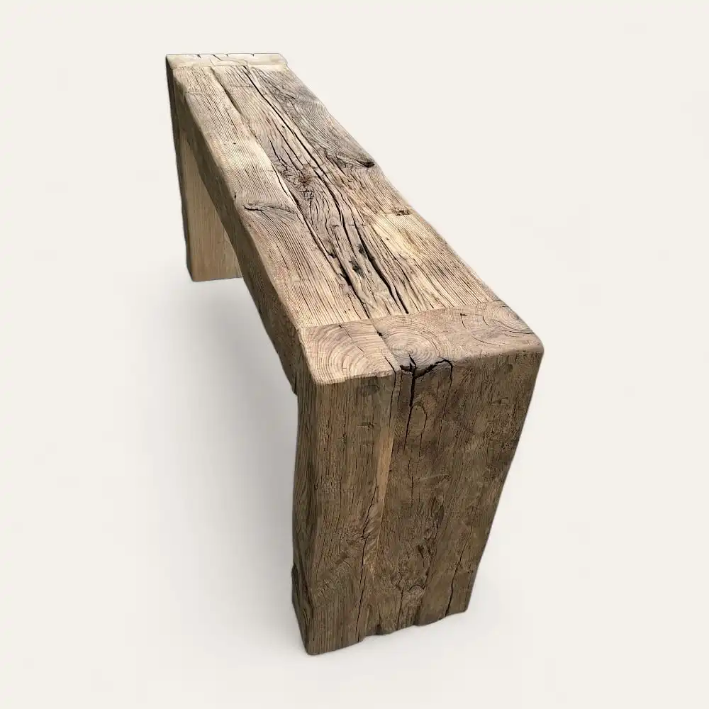  Un banc en bois rustique et patiné avec des fissures visibles et une texture rugueuse, rappelant une console en bois ancien, est posé sur un fond clair. 