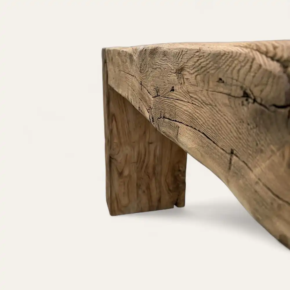  Gros plan d'un pied et d'un côté de table en bois rustique, mettant en valeur la texture du bois naturel et les motifs de grain d'une console en bois ancien sur un fond clair uni. 