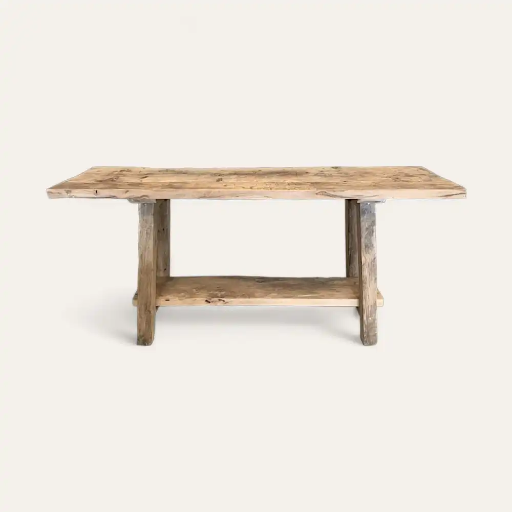  Une table rustique en bois avec un plateau rectangulaire et une étagère en dessous, rappelant une console en bois ancien, sur un fond blanc uni. 