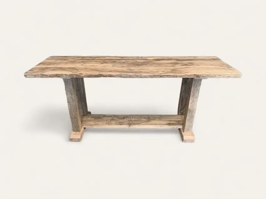 Une table rectangulaire en bois au fini rustique, dotée d'une base à tréteaux des deux côtés. Cette console en bois ancien présente un aspect clair et patiné.