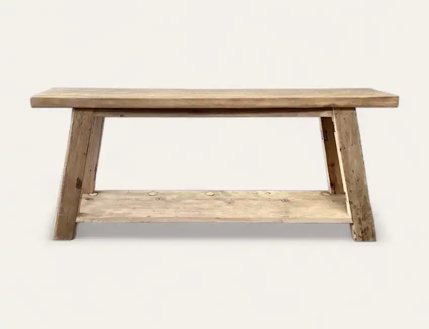 Un banc en bois rustique avec un dessus plat et des pieds inclinés, rappelant une console en bois ancien, doté d'une étagère inférieure supplémentaire pour le rangement.