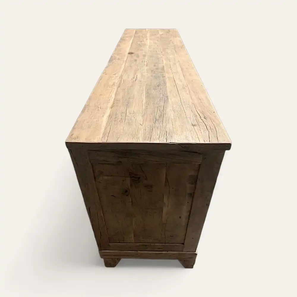  Une table en bois longue et étroite avec une finition claire et naturelle. La table a des pieds carrés et un design minimaliste, rappelant un meuble en bois ancien, présenté sous une vue latérale inclinée. 