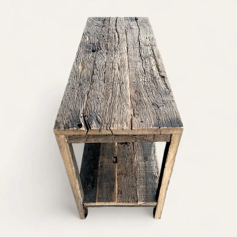  Une table en bois rustique avec un grain visible et des imperfections naturelles, dotée d'une étagère ouverte en dessous. Ce meuble en bois ancien a un aspect naturel patiné et semble être fabriqué à partir de bois de récupération. 