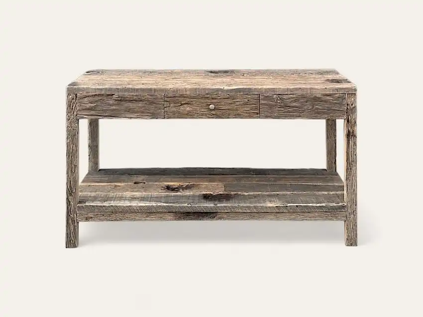 Une table rustique en bois avec un tiroir et une étagère inférieure ouverte, fabriquée à partir de bois de récupération avec une finition patinée, rappelant le meuble en bois ancien.
