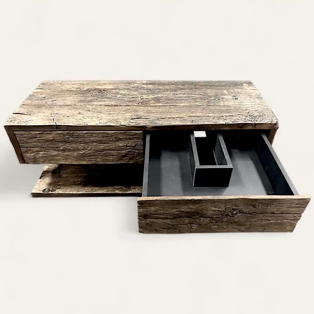  Une table basse rustique en bois avec un tiroir coulissant partiellement ouvert, révélant un intérieur noir avec des compartiments – rappelant un meuble de salle de bain rustique. 