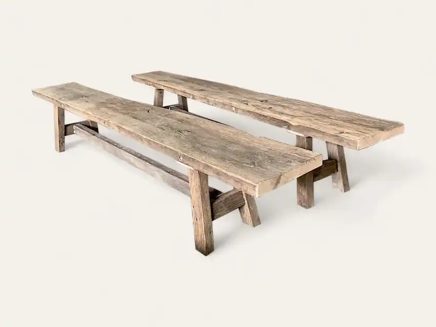 Deux longs bancs rustiques aux surfaces en bois patiné et aux designs simples et robustes reposent sur un fond blanc uni, dégageant un charme ancien.