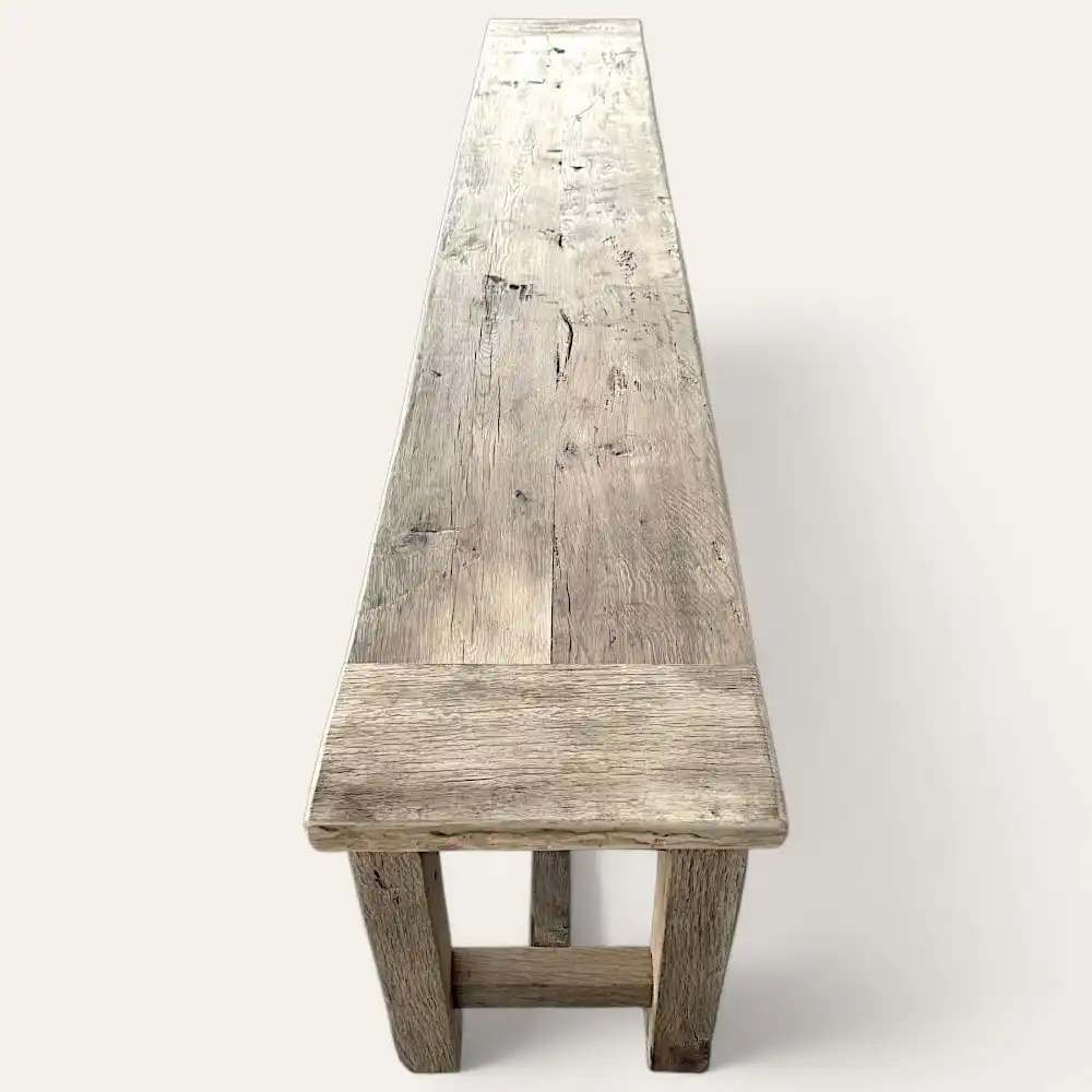  Un long banc rustique en bois avec une usure visible et un aspect patiné se dresse sur un fond clair et uni, incarnant le charme d'un banc rustique classique. 