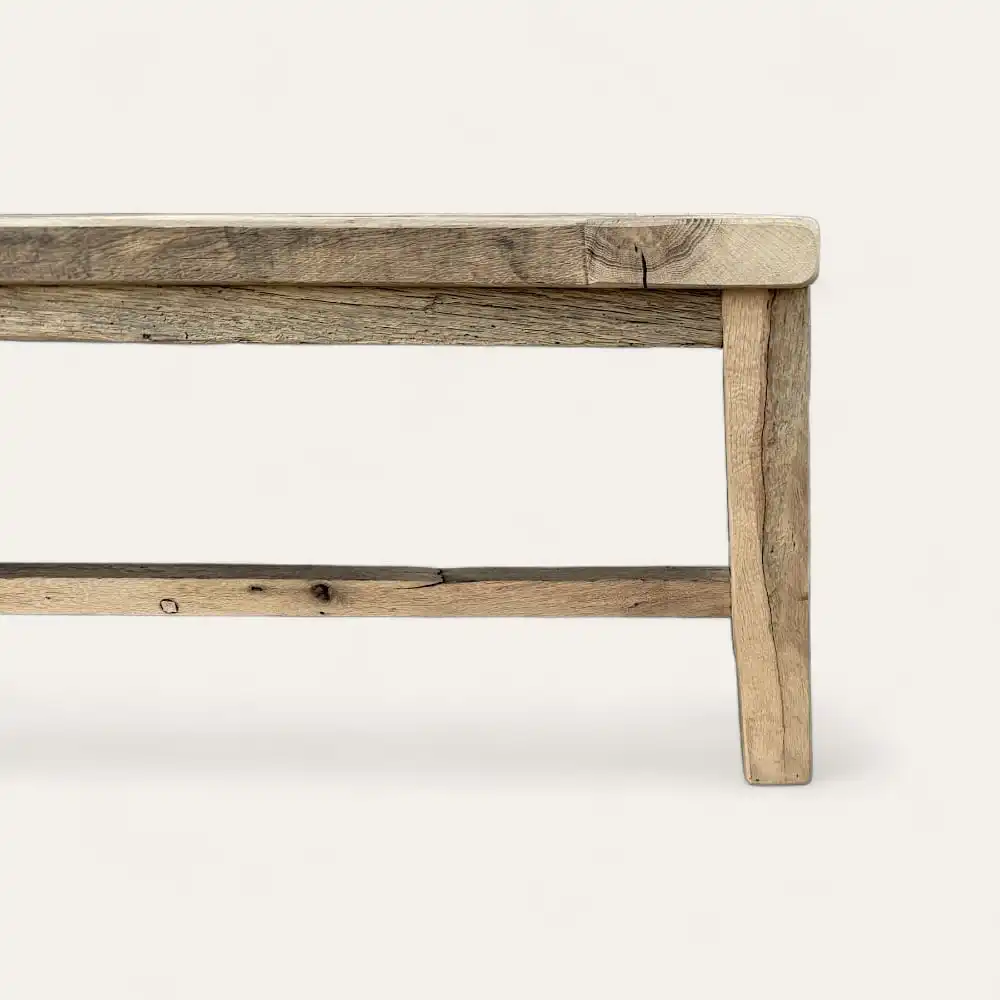  Un banc rustique en bois, ou banc rustique, au design simple, doté d'un siège plat et de quatre pieds robustes. Le banc semble être en bois patiné. 