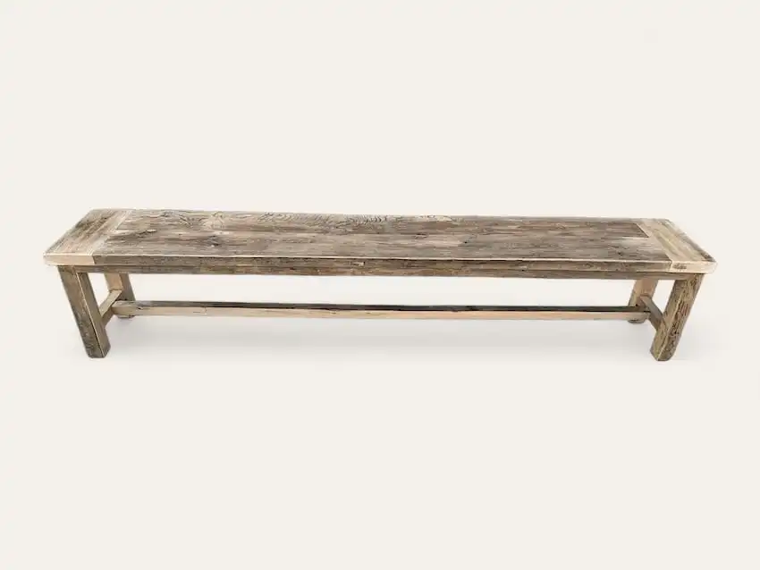 Un long banc rustique en bois avec une finition patinée et des pieds robustes sur un fond blanc uni capture le charme intemporel d'un *banc rustique* classique.