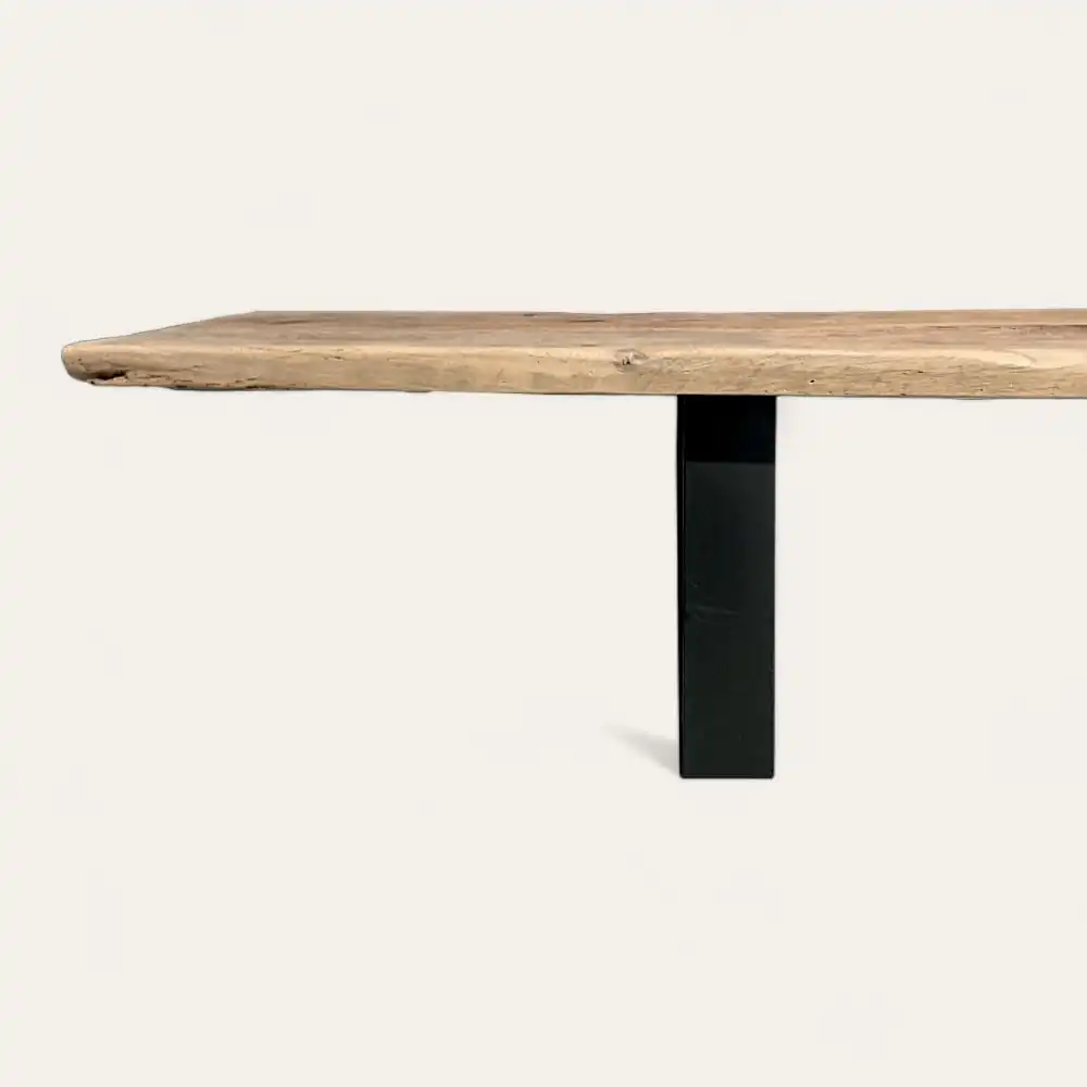  Plateau de table en bois au bord naturel soutenu par un pied en métal noir, rappelant un banc bois ancien, vu sur un fond blanc uni. 