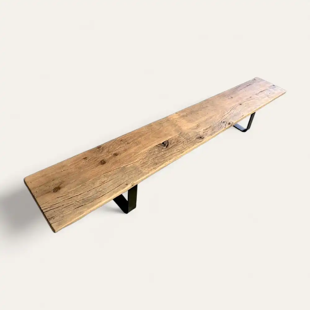  Un long banc en bois au fini naturel et aux pieds en métal noir, rappelant un banc bois ancien, présenté sur un fond uni. 