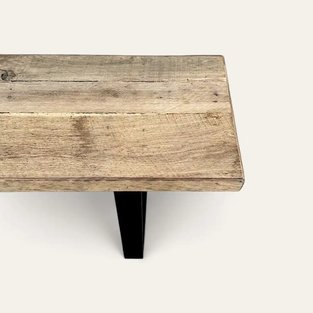  Gros plan d'un coin table en bois à la finition naturelle et rustique, rappelant un banc d'entrée vintage. La table repose élégamment sur des pieds en métal noir. 