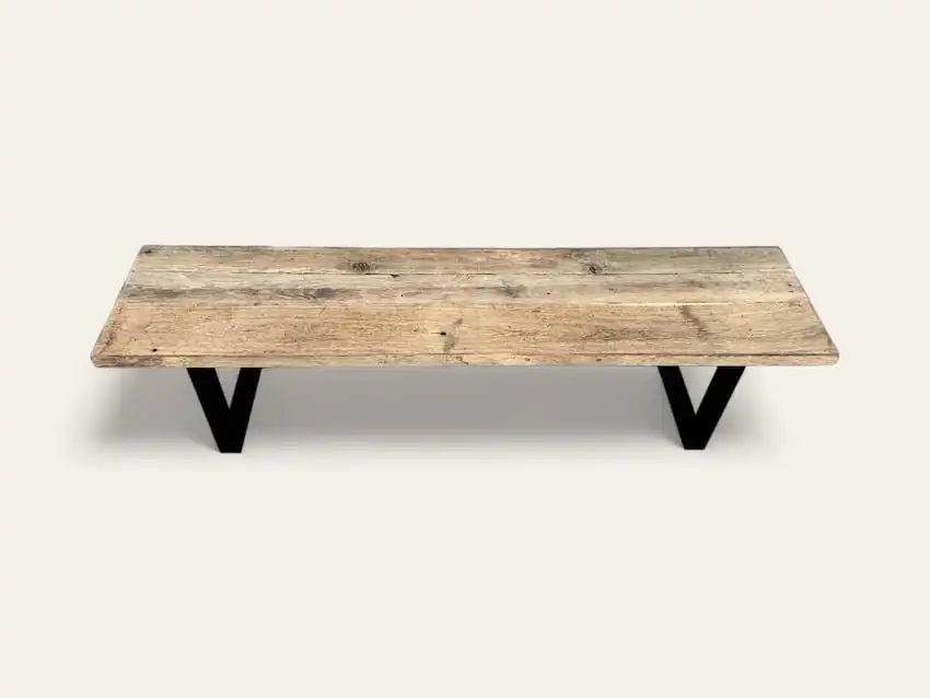 Table basse rectangulaire en bois au fini rustique et pieds en métal noir en forme de V, rappelant un style banc bois ancien.