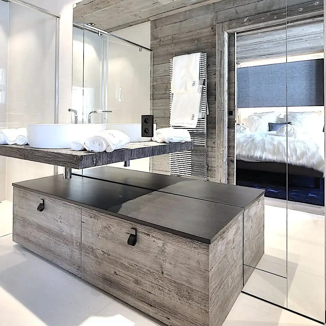  Salle de bain moderne avec vanité rustique en bois faite de panneau 3 plis vieux bois, double vasque, grand miroir et vue sur une chambre attenante avec un lit moelleux. 