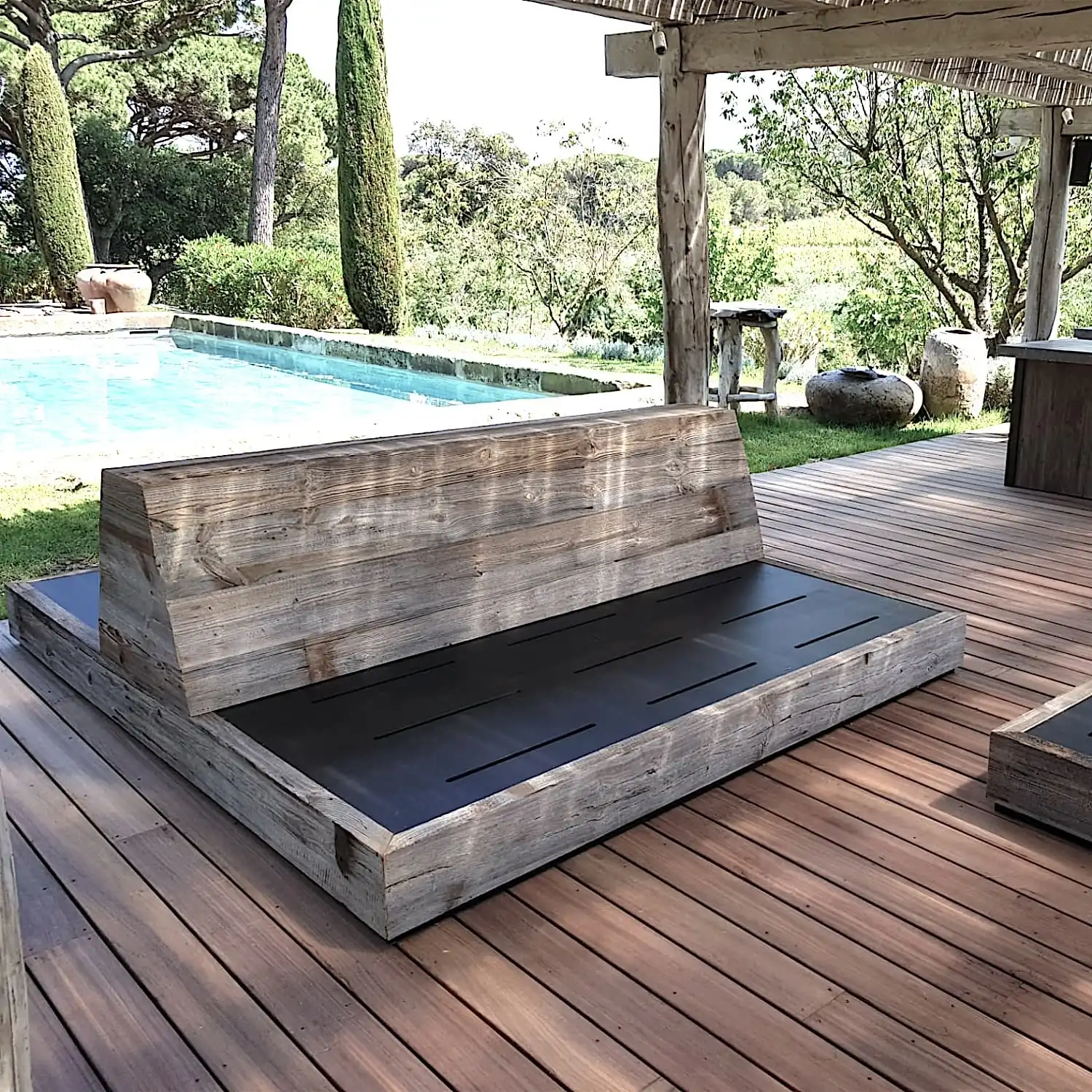  Banc d'extérieur en bois sur une terrasse au bord d'une piscine, entouré d'une verdure luxuriante et agrémenté d'un panneau 3 plis vieux bois. 