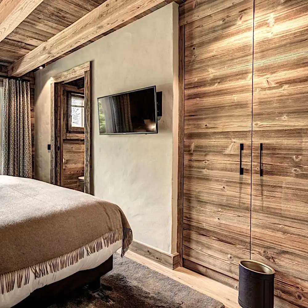 Une chambre confortable avec des murs en bois et un sol en panneaux de bois vieux, avec une télévision à écran plat montée en face du lit et une décoration minimaliste. 