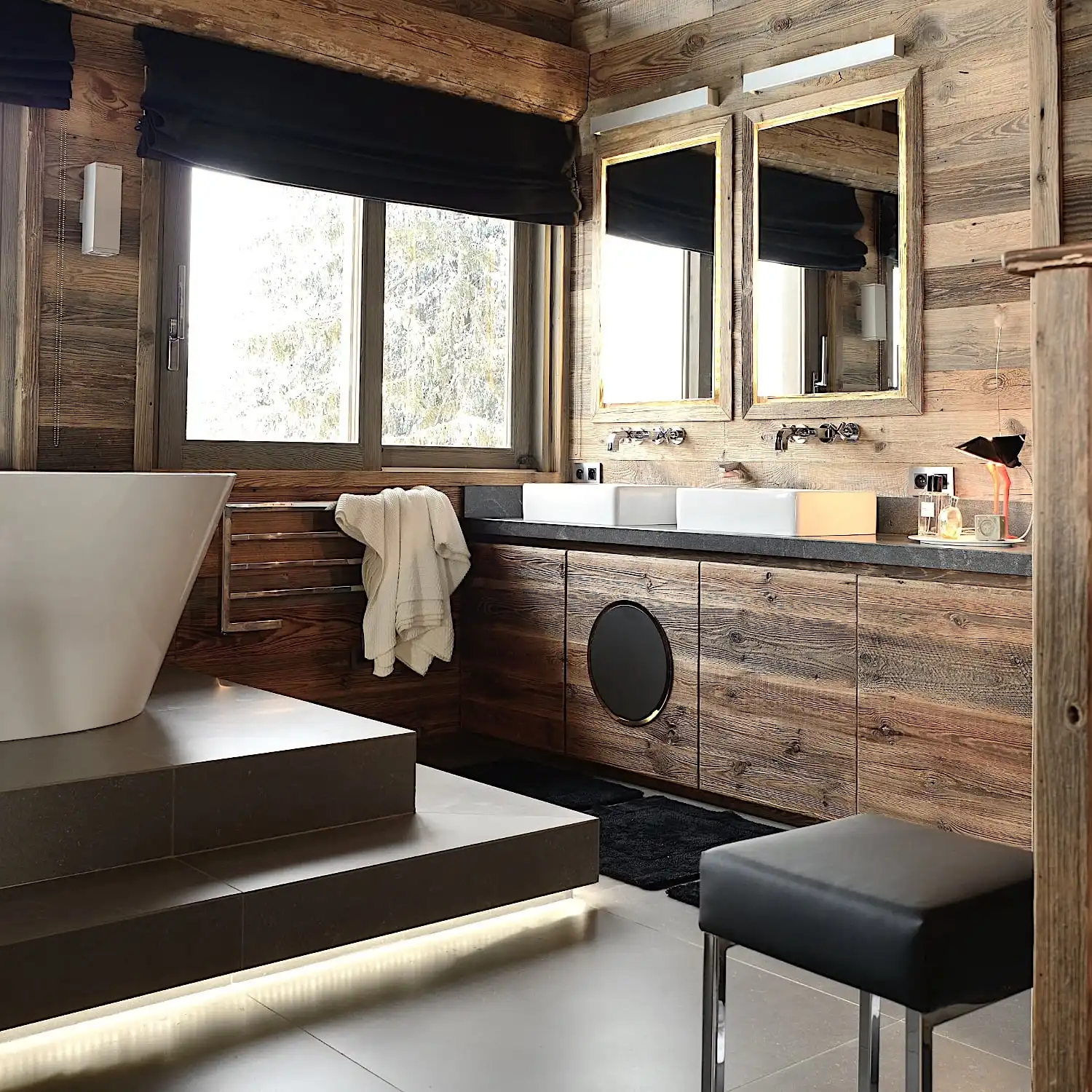  Une luxueuse salle de bains en bois comprenant une baignoire autoportante, des lavabos jumeaux, des luminaires modernes et une vue enneigée à l'extérieur de la fenêtre lambrissée de 3 plis vieux bois. 
