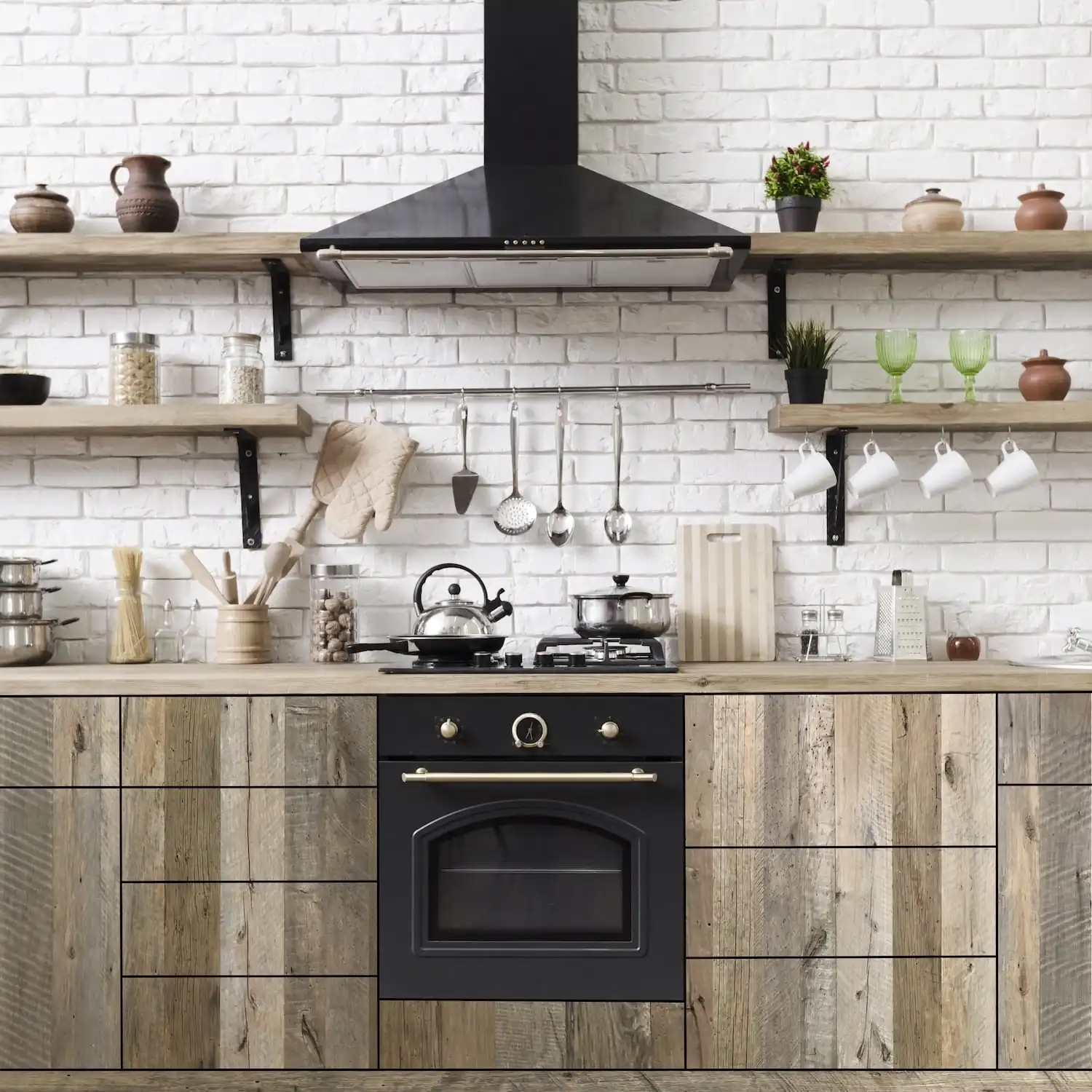  Intérieur de cuisine moderne avec poêle noir, armoires en bois et dosseret carrelé blanc, avec ustensiles suspendus et étagères avec pots et verdure sur panneaux vieux bois. 