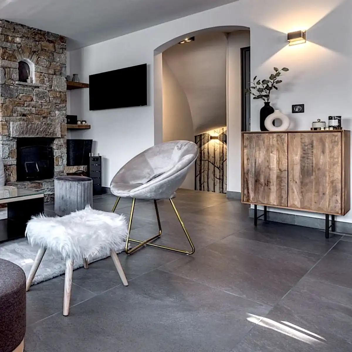  Salon moderne avec un mur en pierre, comprenant une chaise moelleuse, une armoire en bois, un tabouret moelleux et un poêle à bois à panneau 3 plis. 