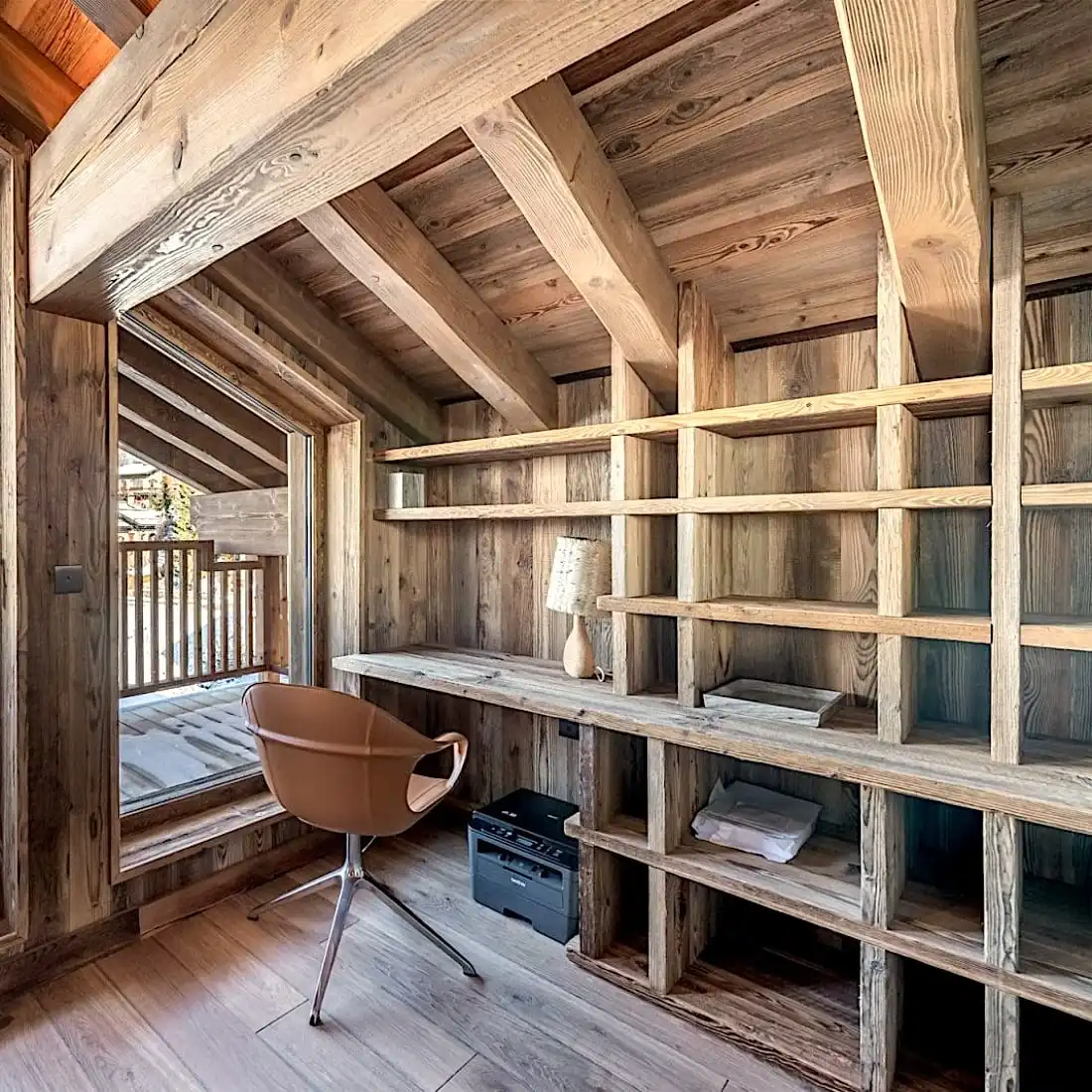  Un intérieur de cabine rustique et confortable comprenant une grande étagère, une chaise moderne et une porte à panneau 5 plis offrant une vue sur le balcon. 
