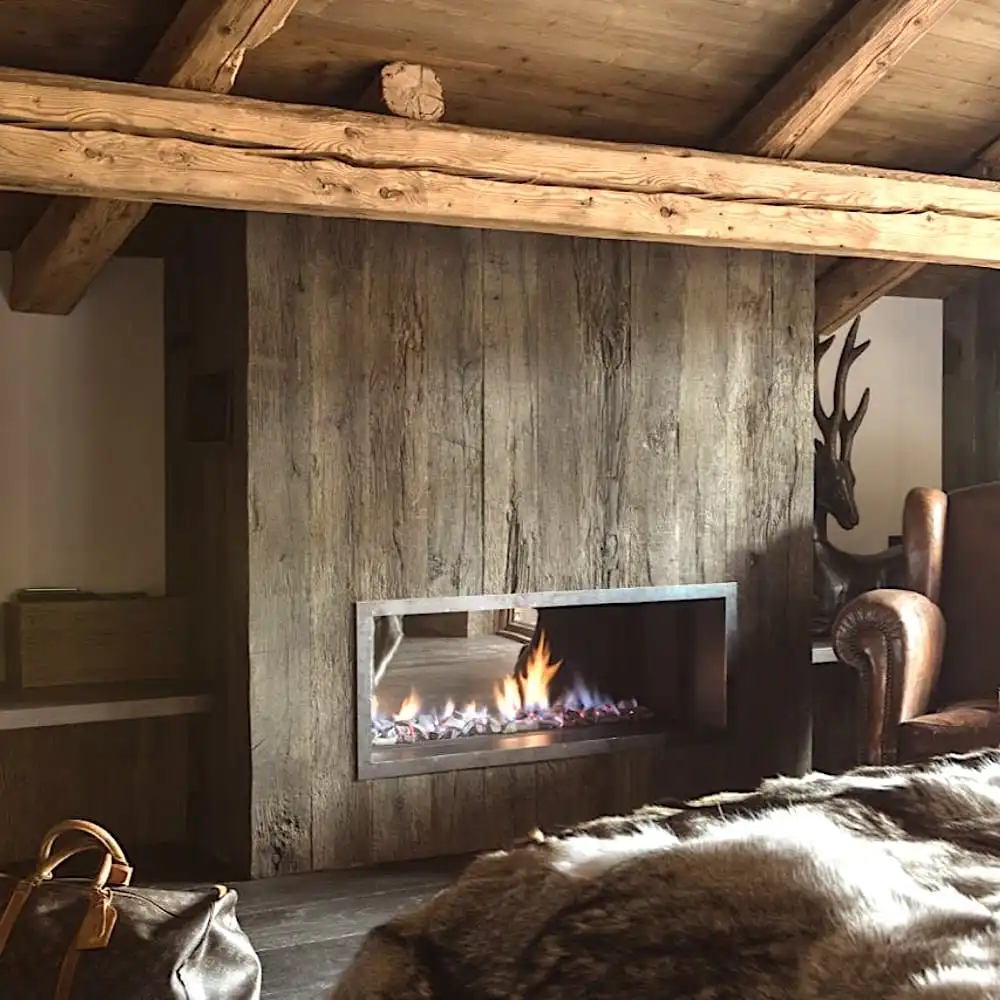  Une salle chaleureuse et rustique avec des poutres en bois, une cheminée moderne encastrée dans un mur en panneaux de vieux bois, des meubles en cuir et une couverture en fourrure. 