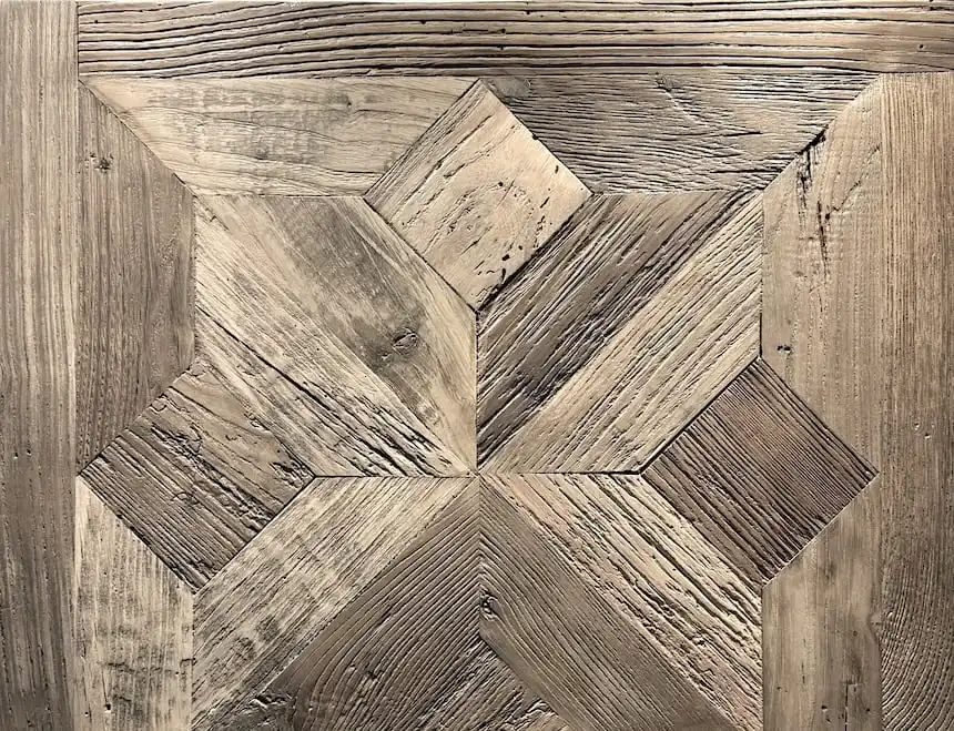 Gros plan d'une surface en bois vieilli avec un motif de parquet géométrique montrant des grains de bois visibles et des marques d'usure, avec un motif de parquet en panneau étoile.