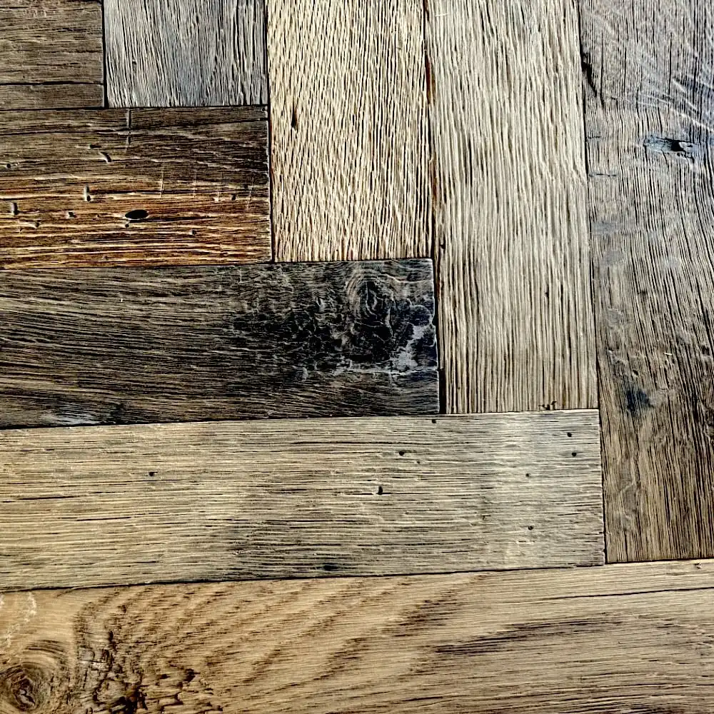  Vue rapprochée d'un plancher en bois avec un motif à chevrons, mettant en valeur diverses nuances et textures de planches de bois, rappelant un plancher ancien. 