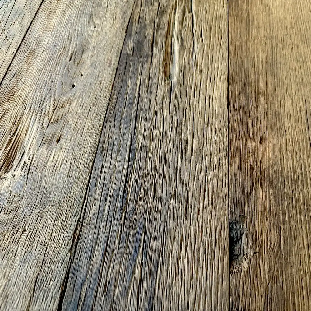  Gros plan de planches de bois vieillies et patinées avec grain et texture visibles. Le bois semble brut et rustique, présentant des imperfections et des usures naturelles, rappelant un plancher ancien. 