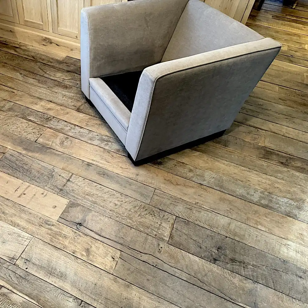  Un fauteuil gris repose sur le plancher ancien dans une pièce avec des armoires en bois clair. 