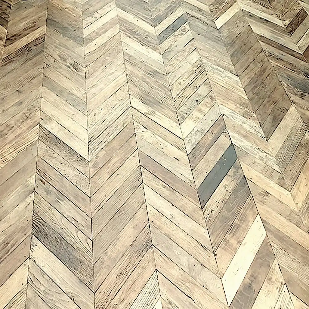  Un plancher ancien avec un motif à chevrons composé de planches de bois de différentes nuances de brun. 