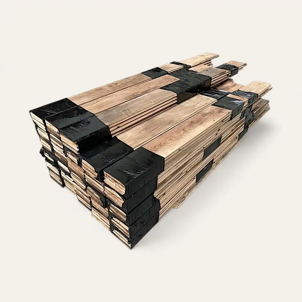  Un empilement de planches de bois, rappelant le parquet ancien châtaignier, fixées par des sangles en plastique noir, posées sur un fond uni blanc. 