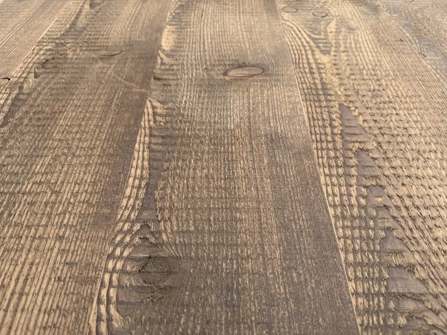 Gros plan d'une surface en bois texturée avec des motifs de grain visibles et des imperfections naturelles. Le bois, qui rappelle le parquet ancien, présente un aspect patiné et rustique proche du sapin vieilli.