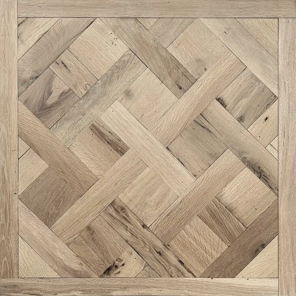  L'image montre un gros plan d'un parquet en bois avec un motif à chevrons. Les pièces de bois de couleur claire sont disposées dans un cadre carré, évoquant l'élégance classique d'un panneau Versailles ancien. 