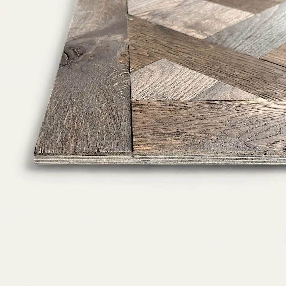  Gros plan d'un carrelage en bois avec un motif à chevrons, présentant des nuances variées de brun et une texture patinée rappelant le parquet de Versailles. Le bord du carreau montre sa construction en couches. 
