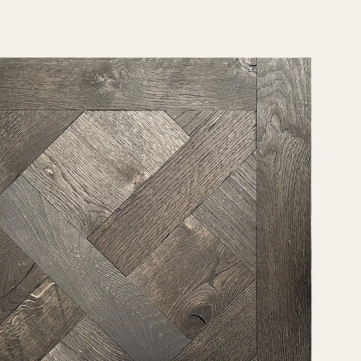  Gros plan d'un parquet en bois avec un motif à chevrons, mettant en valeur la texture et le grain du bois vieilli. L'image met en valeur un détail de l'angle du sol qui rappelle le parquet à panneaux Versailles. 