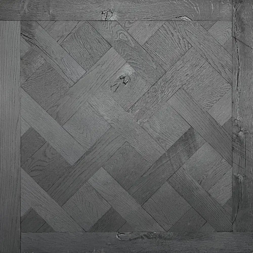  Section carrée de parquet noir en bois gris foncé avec un motif à chevrons rappelant Versailles et un grain de bois visible. 