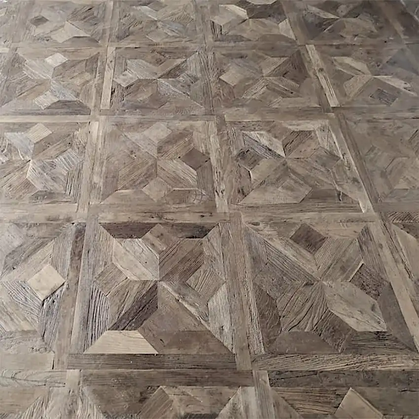  Un parquet en bois avec un motif géométrique de carrés imbriqués, chacun composé de tons de bois plus clairs et plus foncés créant un effet texturé et dimensionnel, rappelant les motifs complexes du parquet étoile traditionnel à panneaux. 