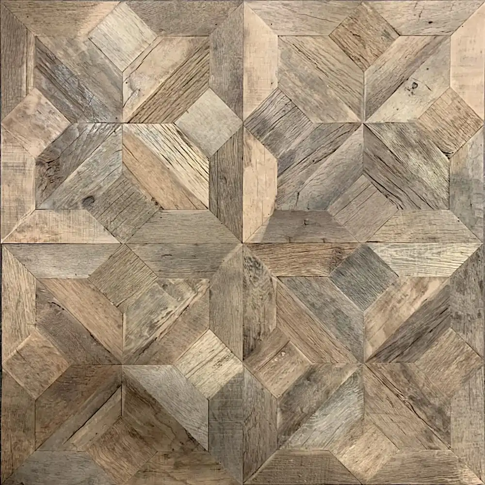  Vue rapprochée d'un parquet en bois avec un motif géométrique complexe, composé de différentes nuances de pièces de bois marron et gris disposées de manière symétrique, rappelant le parquet étoile classique. 