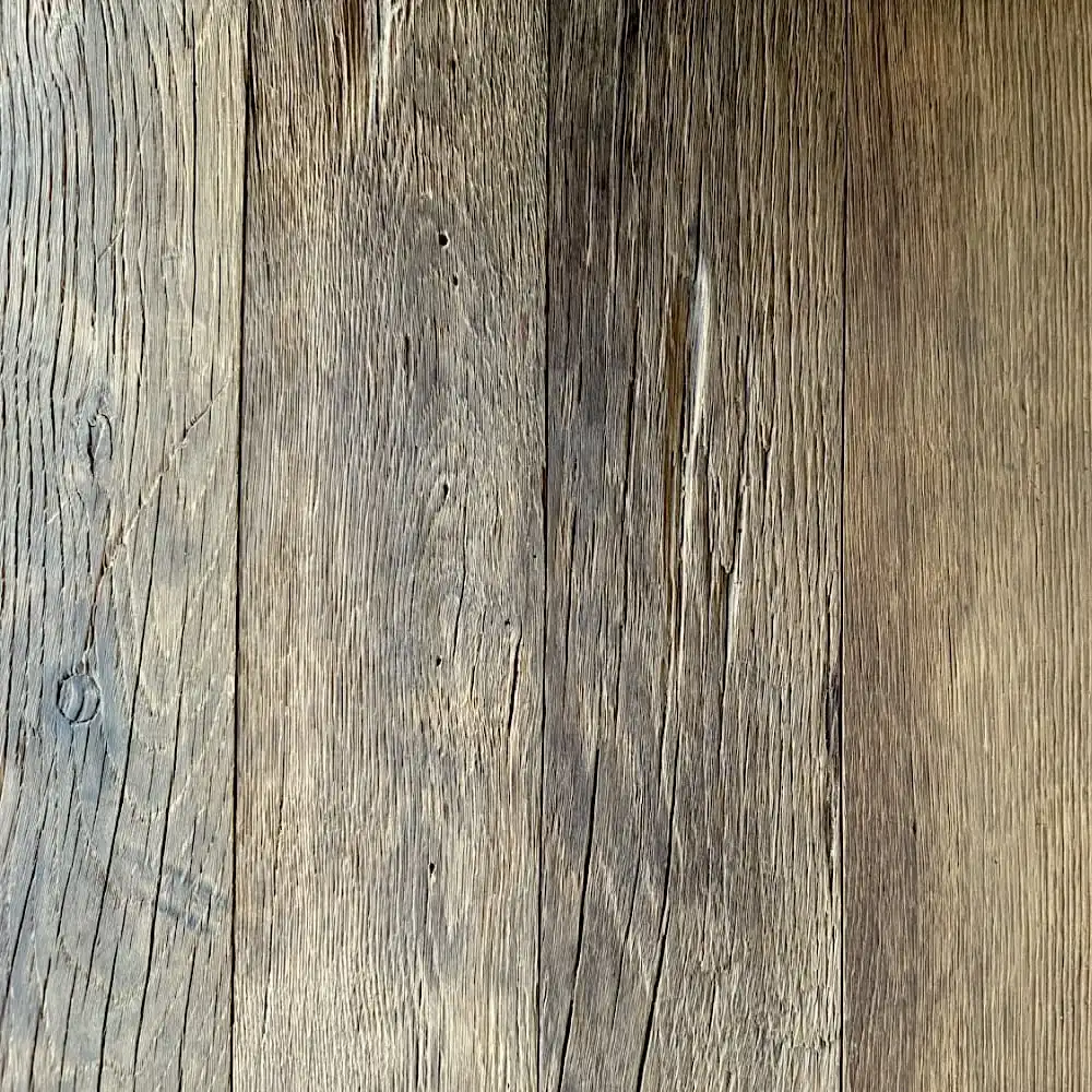  Gros plan d'une surface en bois patinée avec des motifs de grain distincts et différentes nuances de brun, rappelant le parquet ancien. Les planches présentent des textures naturelles et de charmantes irrégularités. 