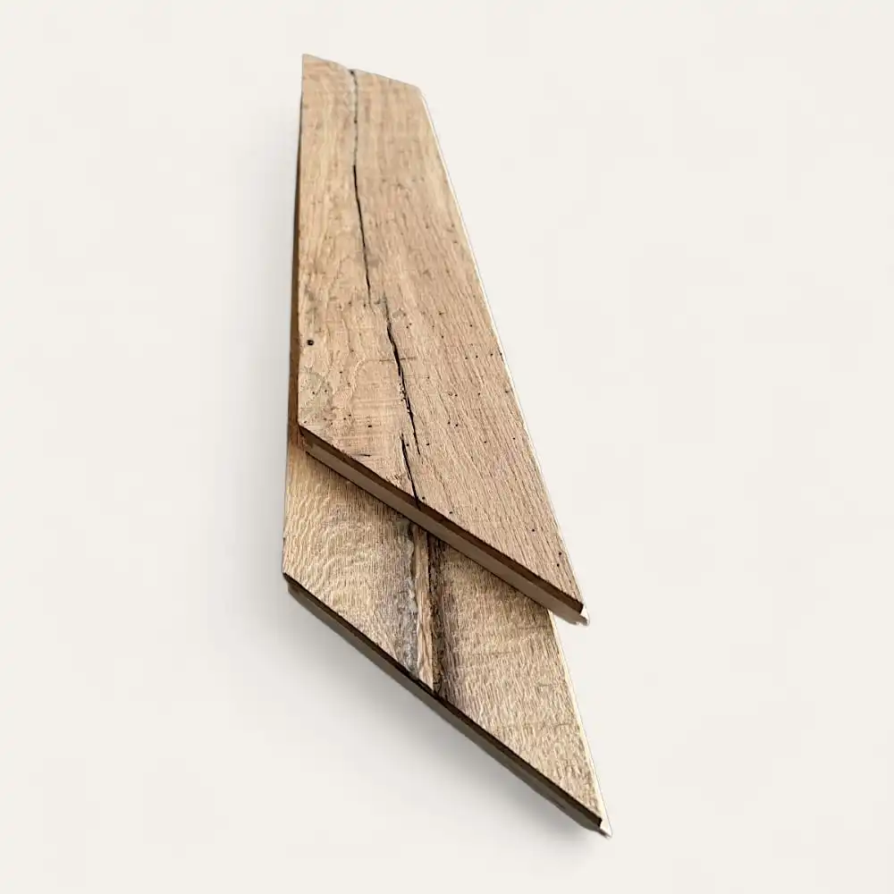  Deux pièces triangulaires de bois brut, présentant des veines et des fissures visibles, sont placées côte à côte sur un fond uni et blanc, rappelant un parquet ancien. 
