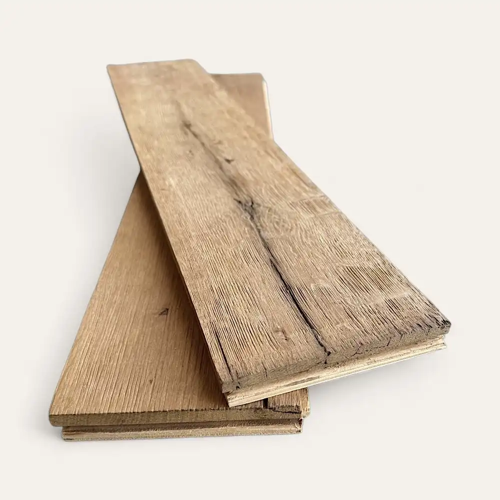  Deux morceaux de parquet en planches de bois, empilés à peu près perpendiculairement l'un à l'autre, avec des textures de grain et de nœuds visibles, rappelant le parquet ancien classique, sur un fond blanc uni. 